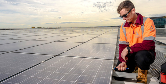 man in hi vis inspecting solar panels on roof